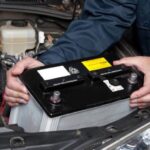 An image showing a man holding a car battery.